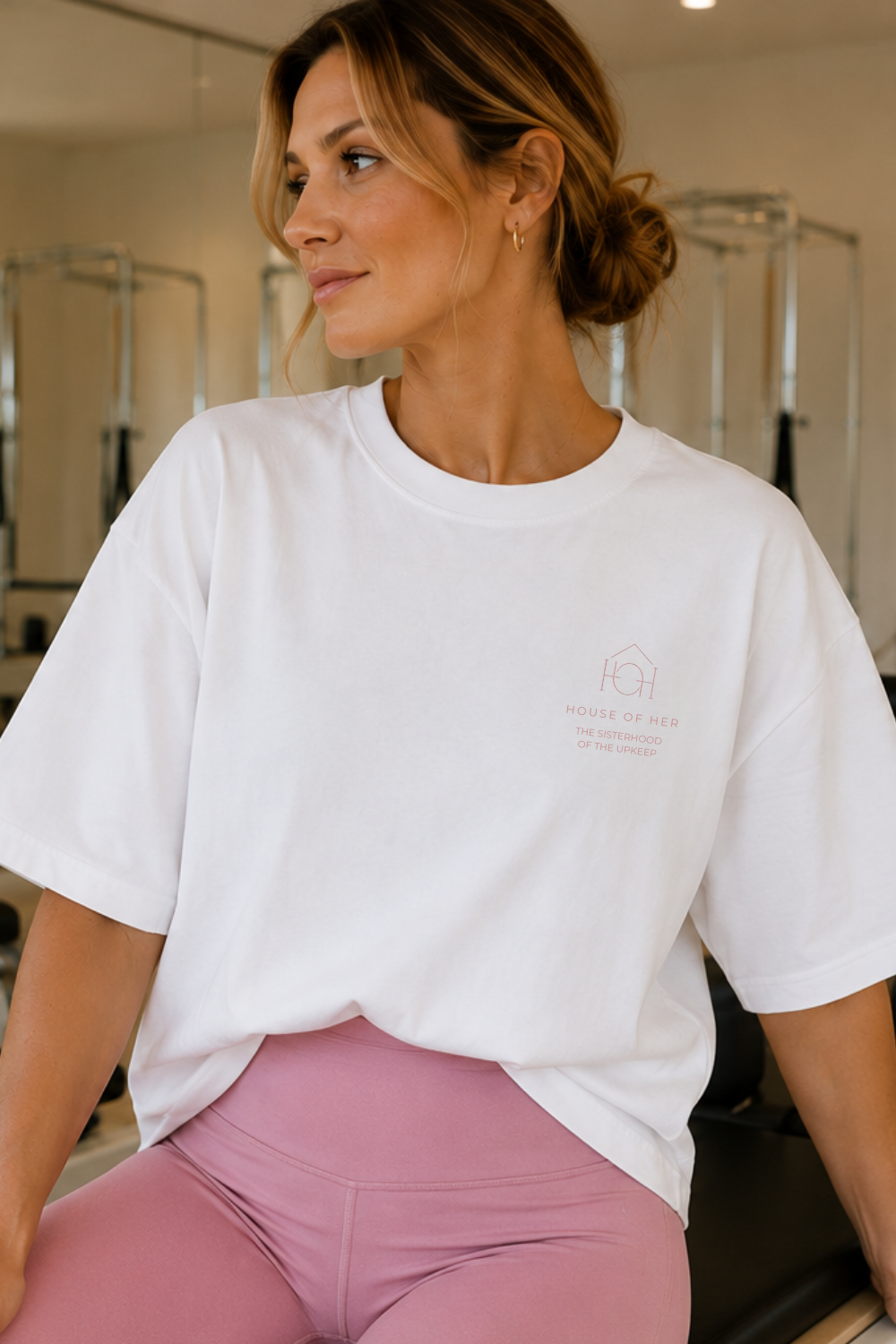 Woman wearing a white t-shirt with a logo and pink pants in a gym setting